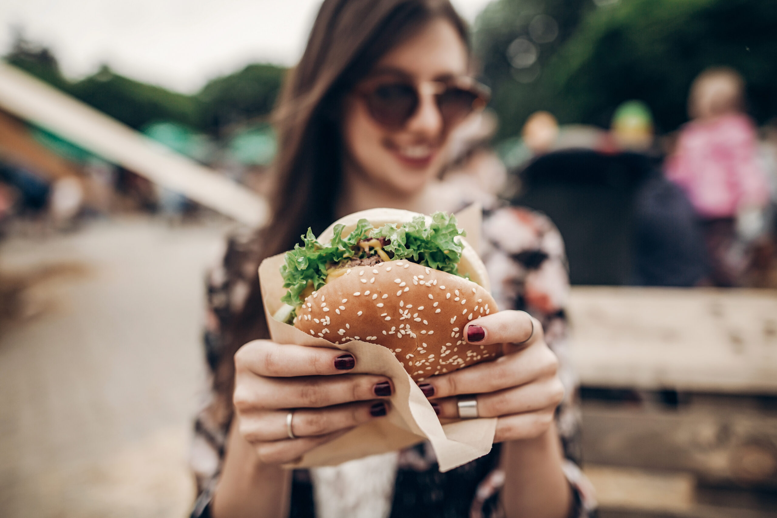 tasty burger. stylish hipster woman holding juicy hamburger in hands close up. boho girl with hamburger at street food festival. summertime. summer vacation picnic. space for text
